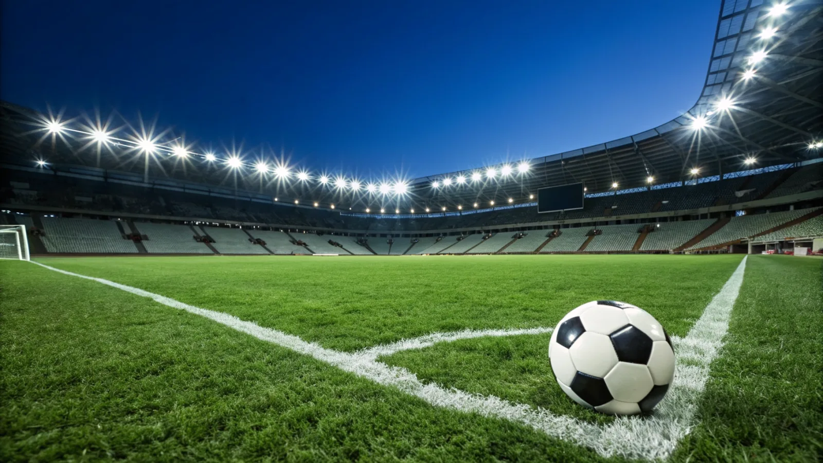 A soccer ball on the pitch of a floodlit stadium at night